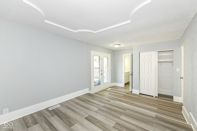 unfurnished bedroom featuring visible vents, baseboards, a textured ceiling, and wood finished floors