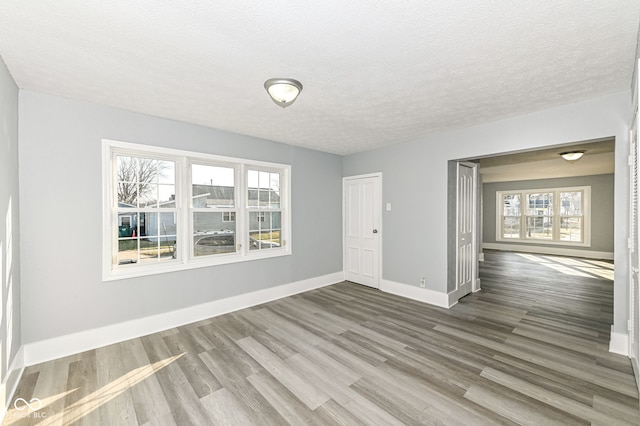 empty room with baseboards, plenty of natural light, a textured ceiling, and wood finished floors