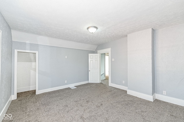 unfurnished bedroom with baseboards, a textured ceiling, lofted ceiling, and carpet