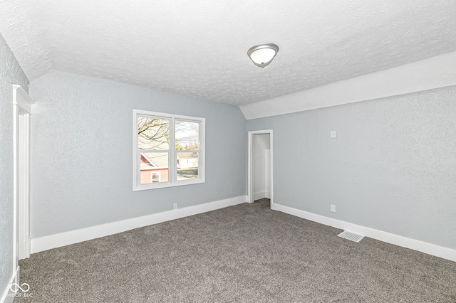 unfurnished room featuring visible vents, a textured ceiling, dark colored carpet, lofted ceiling, and a textured wall