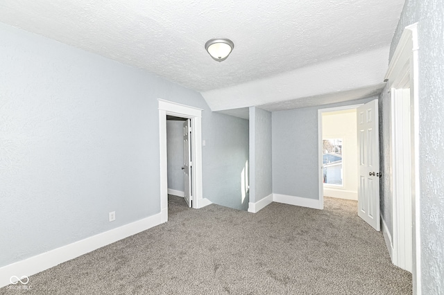 carpeted empty room featuring baseboards, a textured ceiling, and vaulted ceiling