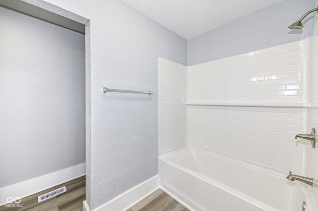 full bathroom with visible vents, shower / washtub combination, a textured wall, and wood finished floors