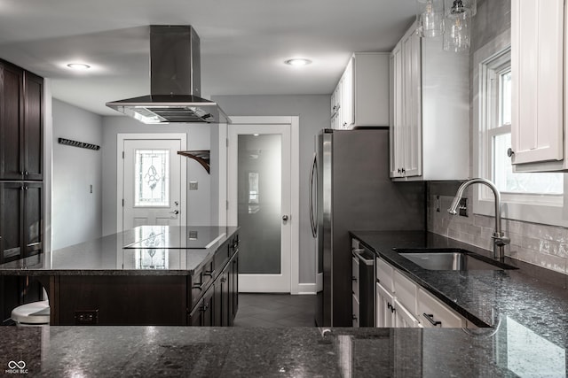 kitchen with tasteful backsplash, dark stone counters, island exhaust hood, white cabinets, and a sink