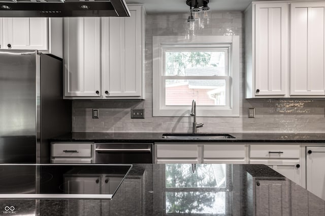 kitchen with white cabinetry, backsplash, freestanding refrigerator, and a sink