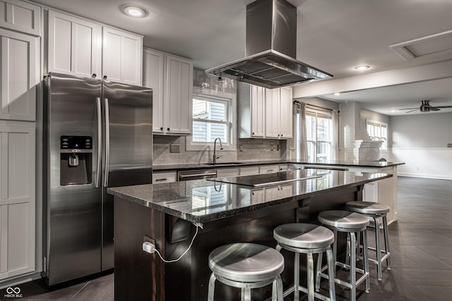 kitchen featuring island exhaust hood, a sink, stainless steel appliances, a peninsula, and decorative backsplash