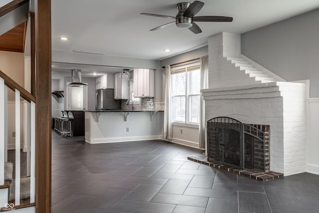 unfurnished living room featuring stairway, a ceiling fan, baseboards, a fireplace, and a sink