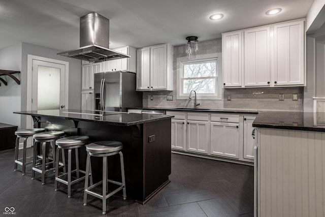 kitchen with a sink, stainless steel refrigerator with ice dispenser, white cabinetry, black electric stovetop, and island range hood