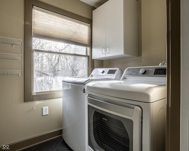 clothes washing area featuring washer and dryer, dark tile patterned floors, cabinet space, and baseboards