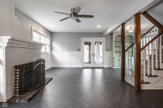 unfurnished living room featuring baseboards, stairway, french doors, a fireplace, and a ceiling fan