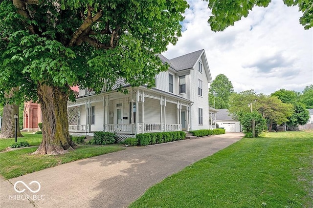 victorian home featuring a porch, an outdoor structure, a detached garage, and a front yard