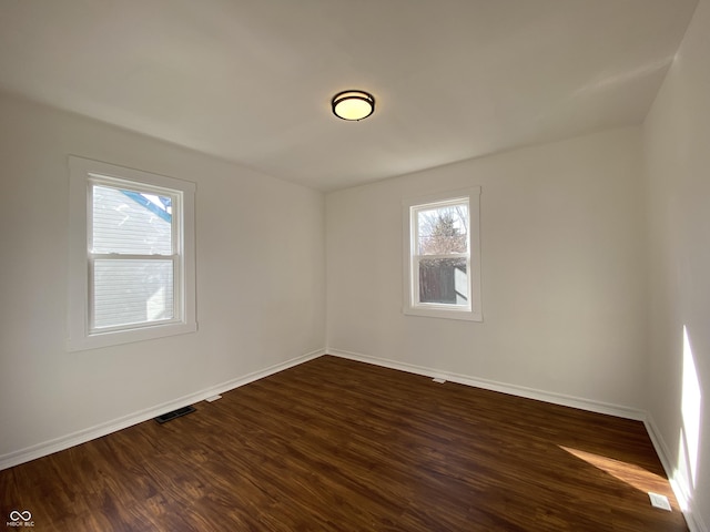 spare room with visible vents, baseboards, and dark wood finished floors