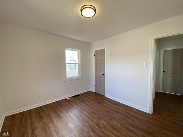 empty room featuring visible vents, baseboards, and dark wood-style flooring