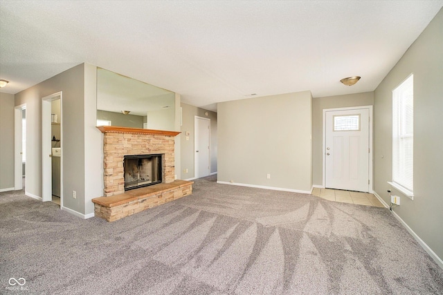 unfurnished living room featuring a stone fireplace, carpet flooring, baseboards, and a textured ceiling