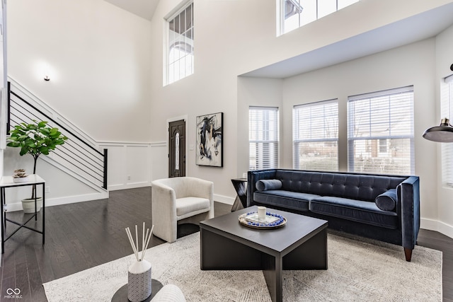 living area featuring stairway, wood finished floors, a towering ceiling, and a healthy amount of sunlight