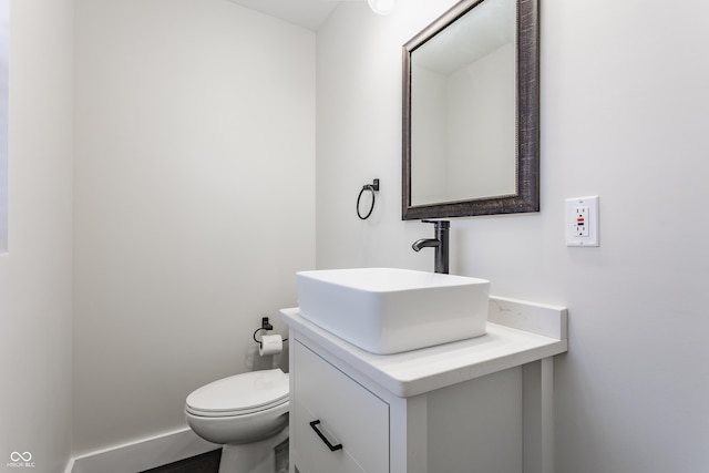 half bathroom with baseboards, toilet, and vanity