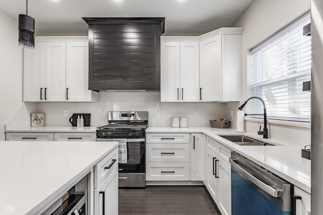 kitchen with a sink, wall chimney range hood, light countertops, appliances with stainless steel finishes, and dark wood-style flooring