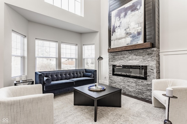 living room featuring a wealth of natural light, a towering ceiling, a fireplace, and a decorative wall