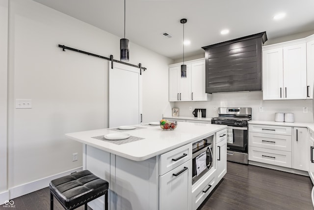 kitchen featuring visible vents, wall chimney range hood, a barn door, stainless steel appliances, and dark wood-style flooring