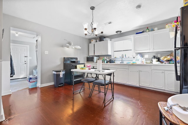 kitchen with dark wood-type flooring, black appliances, a sink, white cabinets, and a chandelier