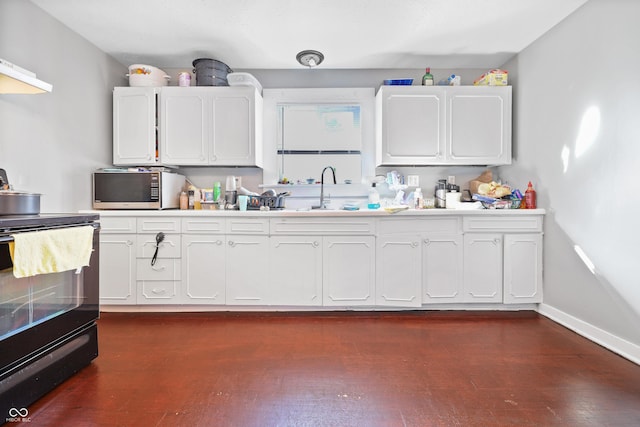 kitchen featuring stainless steel microwave, black range with electric stovetop, dark wood-type flooring, and a sink