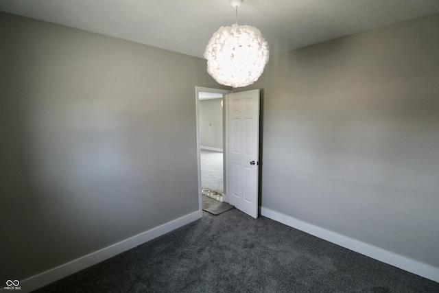 unfurnished room with baseboards, a chandelier, and dark carpet