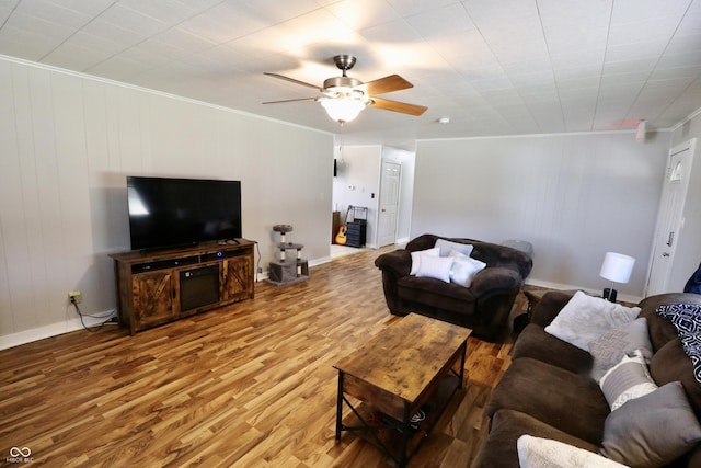 living area with baseboards, crown molding, a ceiling fan, and wood finished floors