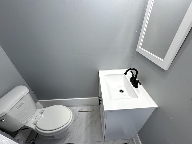 half bathroom featuring baseboards, toilet, marble finish floor, and vanity