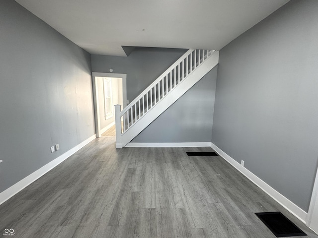 unfurnished living room featuring visible vents, stairway, baseboards, and wood finished floors