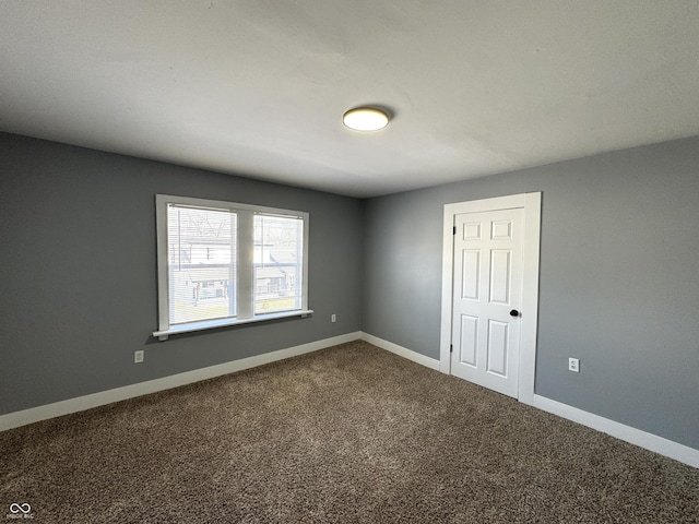 unfurnished room with dark colored carpet and baseboards