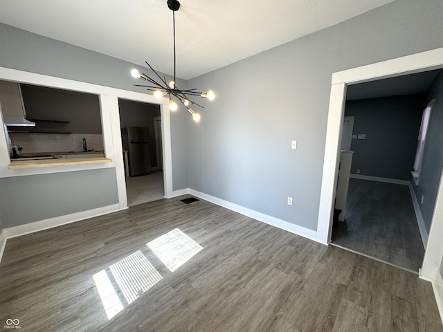 unfurnished dining area featuring wood finished floors, baseboards, and a chandelier