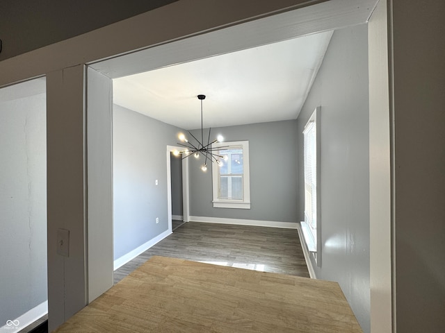 unfurnished dining area with a notable chandelier, baseboards, and wood finished floors