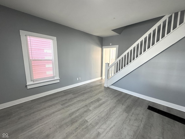 unfurnished living room featuring stairs, baseboards, and wood finished floors