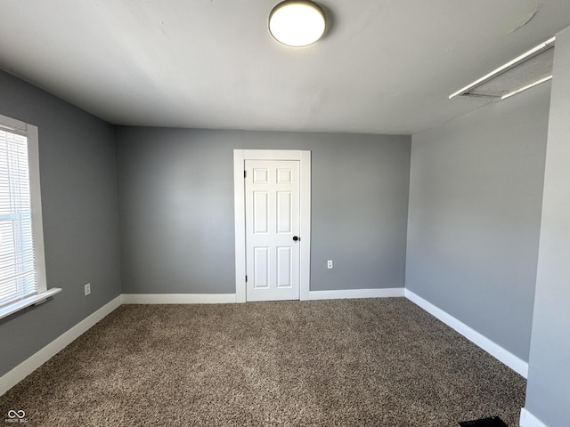 carpeted empty room featuring attic access and baseboards