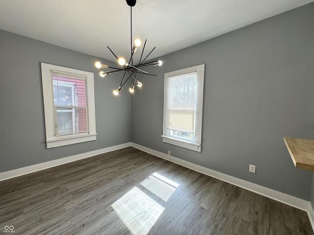 spare room featuring a chandelier, dark wood finished floors, and baseboards