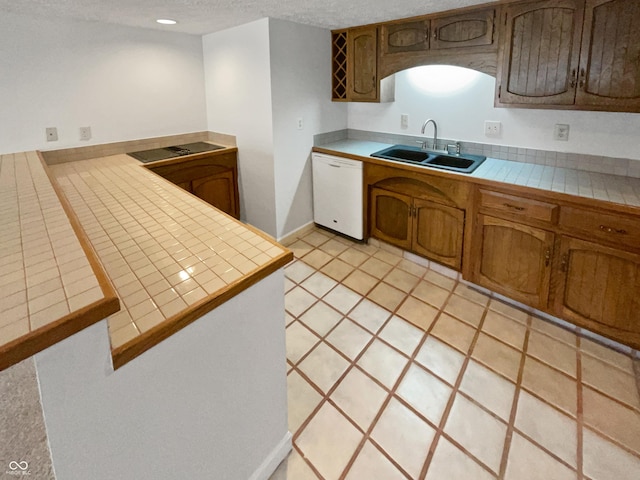 kitchen featuring brown cabinets, a sink, a textured ceiling, dishwasher, and tile counters