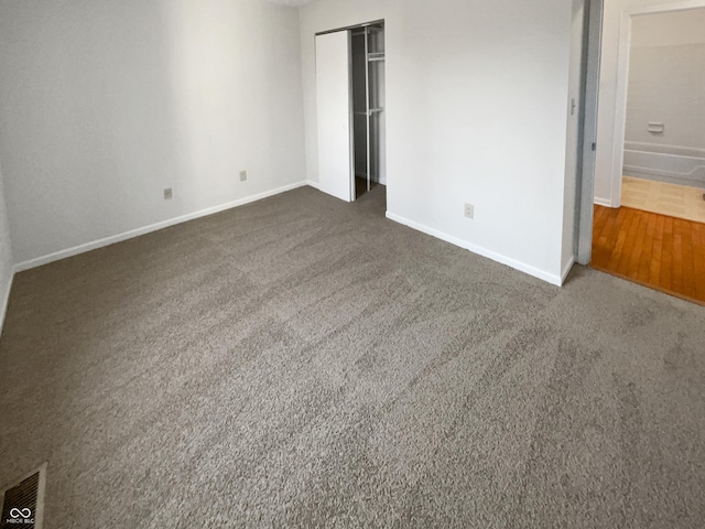 unfurnished bedroom with dark colored carpet, a closet, baseboards, and visible vents