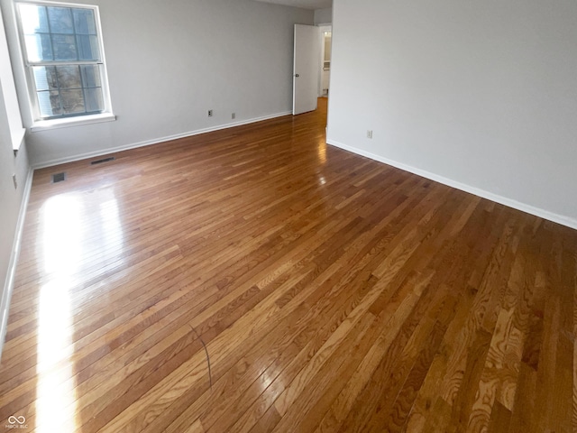 empty room with dark wood-style floors, visible vents, and baseboards