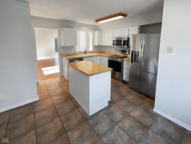 kitchen with butcher block countertops, a sink, white cabinetry, appliances with stainless steel finishes, and baseboards