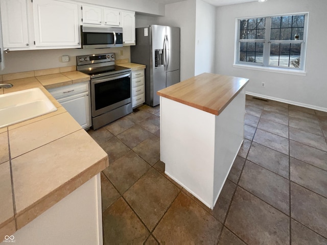 kitchen featuring a kitchen island, a sink, stainless steel appliances, white cabinetry, and butcher block counters