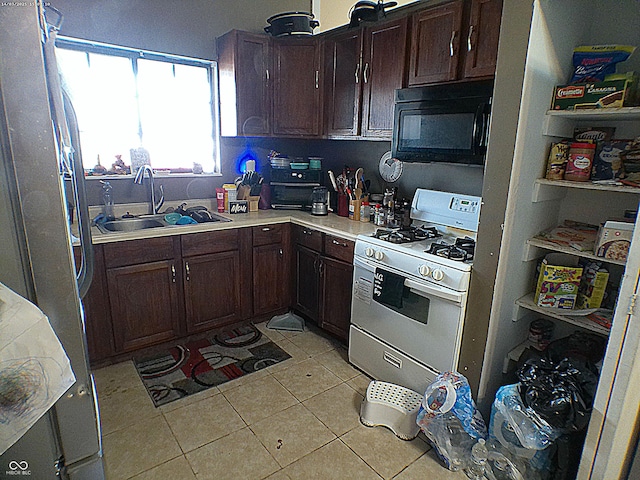 kitchen with light tile patterned floors, white gas stove, freestanding refrigerator, a sink, and black microwave