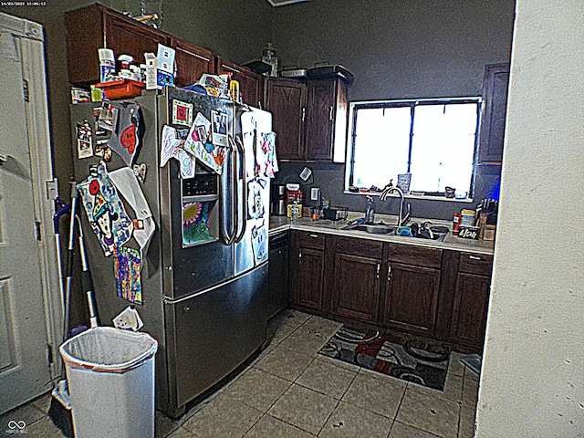 kitchen with dark tile patterned floors, stainless steel refrigerator with ice dispenser, a sink, light countertops, and dark brown cabinets