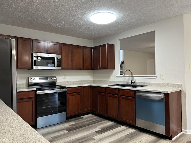 kitchen featuring light wood-style flooring, appliances with stainless steel finishes, light countertops, and a sink