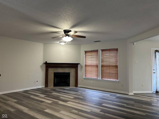 unfurnished living room featuring a ceiling fan, visible vents, baseboards, dark wood finished floors, and a tiled fireplace