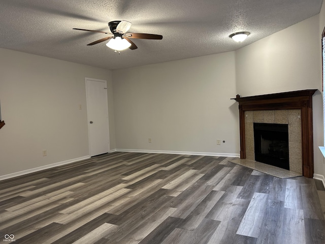 unfurnished living room featuring baseboards, a tile fireplace, ceiling fan, dark wood-type flooring, and a textured ceiling