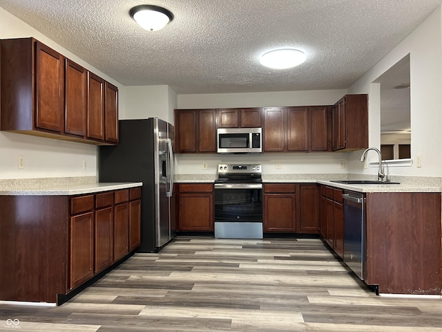 kitchen featuring light wood finished floors, light countertops, appliances with stainless steel finishes, a textured ceiling, and a sink