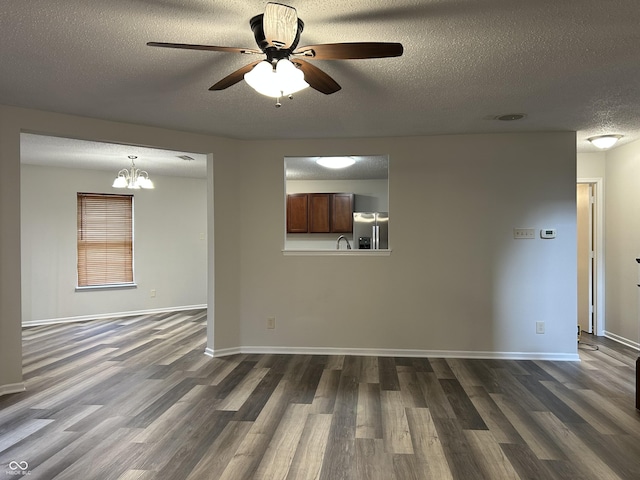 empty room with a textured ceiling, baseboards, dark wood-type flooring, and ceiling fan with notable chandelier