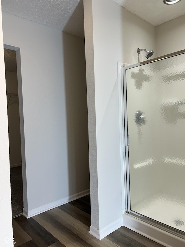 full bath featuring a shower stall, a walk in closet, baseboards, wood finished floors, and a textured ceiling