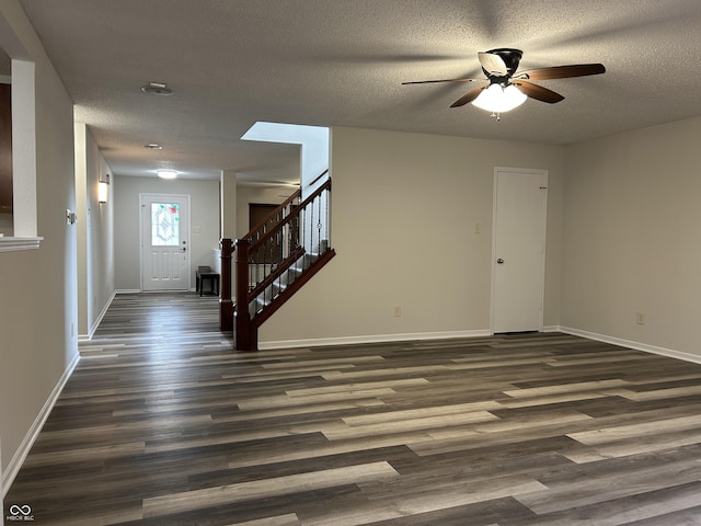 interior space with a ceiling fan, a textured ceiling, dark wood finished floors, baseboards, and stairs