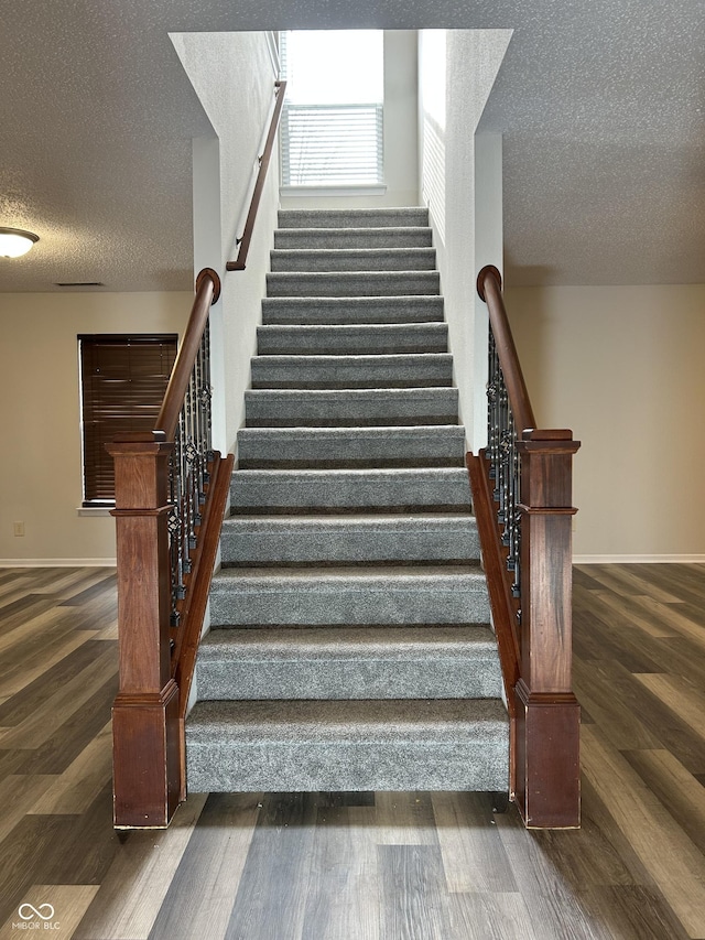 stairs featuring wood finished floors, baseboards, and a textured ceiling