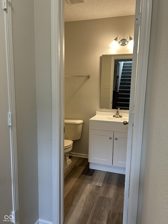 bathroom featuring toilet, a textured ceiling, wood finished floors, vanity, and a textured wall